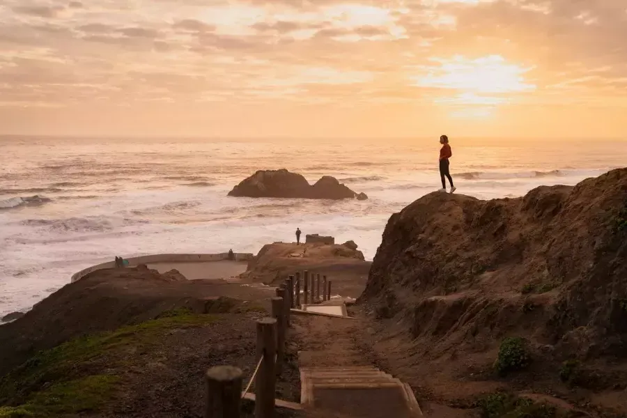 Due persone sono in piedi sulle rocce che si affacciano sull'oceano presso i bagni Sutro di San Francisco.